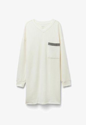 Chemise à manches longues couleur crème avec un col en V, texture à côtes verticales, et une poche poitrine ornée d'un motif à carreaux noir et blanc.