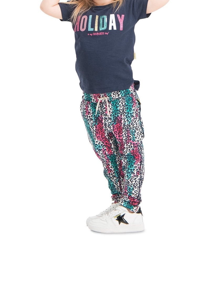 T-shirt marine avec "HOLIDAY" en lettres scintillantes associé à un pantalon de jogging à motifs léopard colorés. Baskets blanches avec un détail en étoile noire.