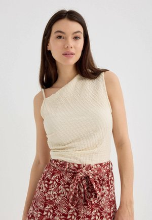Top texturizado de color crema con un solo hombro y tirante delgado, combinado con una falda de cintura alta con estampado de hojas rojas y cintura atada.