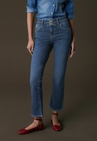 Mörkblå denimjeans med hög midja, fem fickor och metallknappdetaljer. Matchat med röda ballerinas med vita prickar.