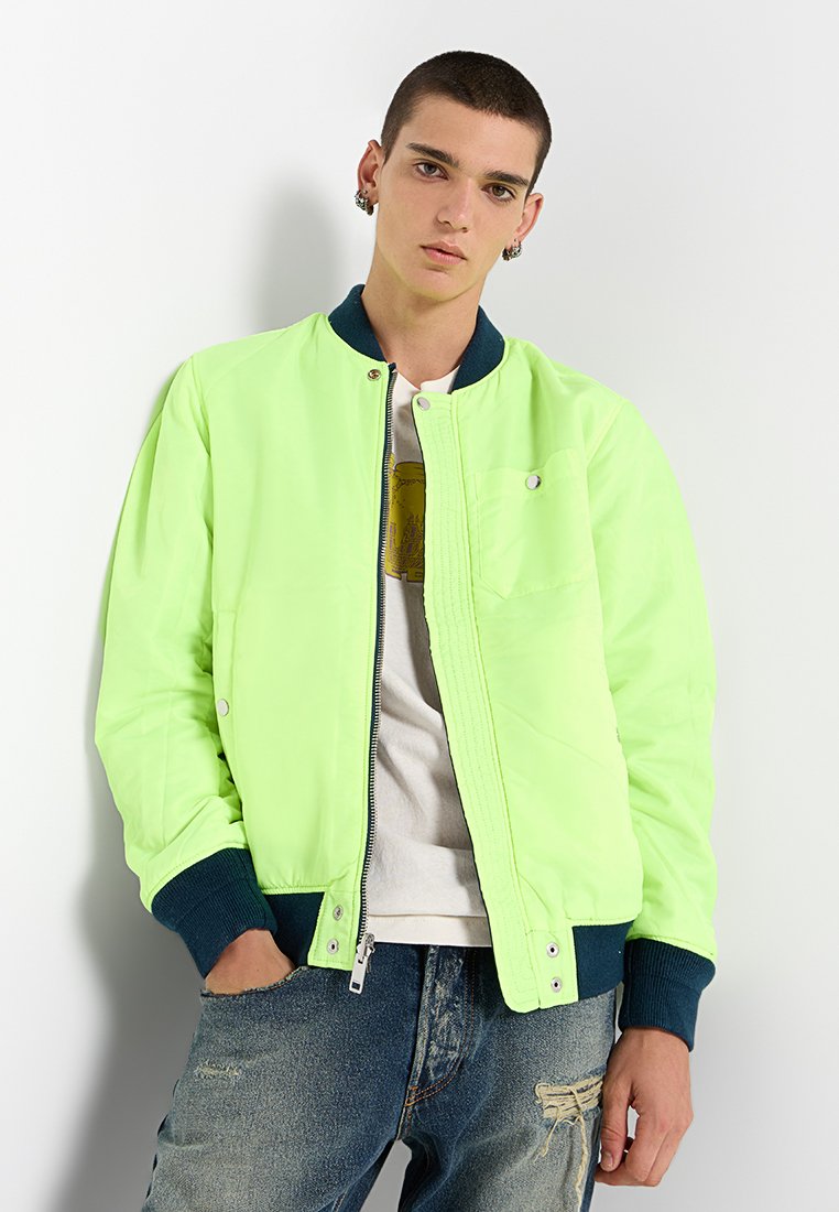 Veste bomber vert néon avec un col et des poignets en maille bleu marine, dotée d'un zip à l'avant, de poches latérales et d'un design simple cousu.