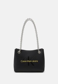 Black handbag made of faux leather, featuring a silver chain strap, embossed logo, and yellow text reading "Calvin Klein Jeans."