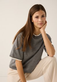 Graumelierter Strickpullover mit rundem Ausschnitt und kurzen Ärmeln, mit weißen Akzenten an Bündchen und Kragen, präsentiert mit cremefarbenen Hosen.