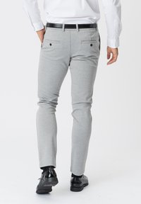 Grå skræddersyede bukser lavet af et glat stof, med en tapered pasform, to baglommer med knapper og sorte dress sko.