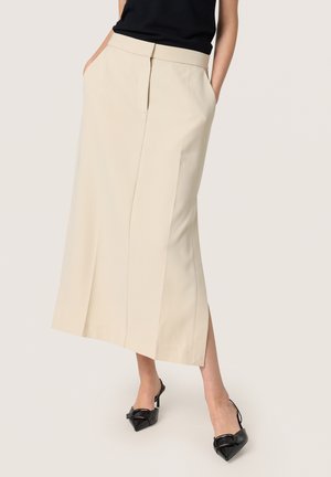 Beige midi rok met een rechte snit, zijzakken en een plissé detail aan de voorkant, gecombineerd met zwarte puntige hakken.