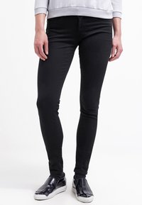Jeans negros ajustados de mezclilla, con una textura suave y un diseño clásico de cinco bolsillos, combinados con zapatos negros sin cordones.