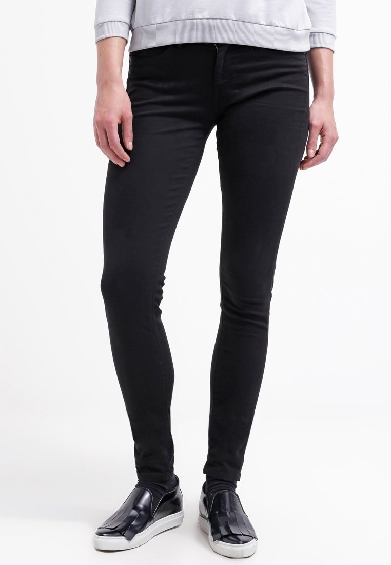 Jeans negros ajustados de mezclilla, con una textura suave y un diseño clásico de cinco bolsillos, combinados con zapatos negros sin cordones.