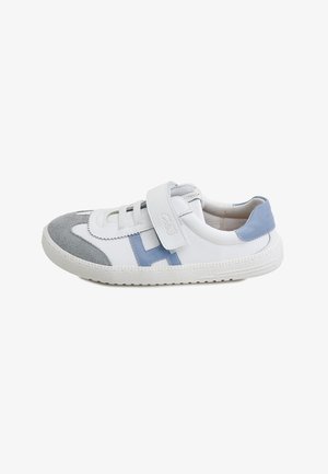 Zapatilla blanca con puntera de ante gris, tacón y detalles laterales en azul, tira de Velcro y suela blanca texturizada sobre un fondo blanco liso.