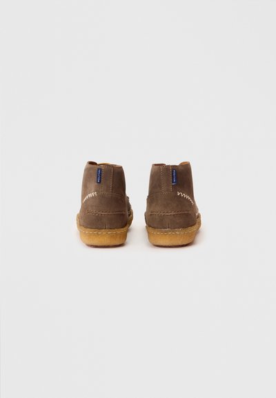 Bottes chelsea en daim marron avec des accents cousus, une semelle en caoutchouc et un design simple et arrondi. Présente une petite étiquette de logo à l'arrière.