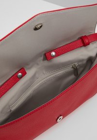 Červená kožená kabelka otevřená, aby odhalila béžovou vnitřní podšívku se zipovou kapsou a cvokem na zavírání.