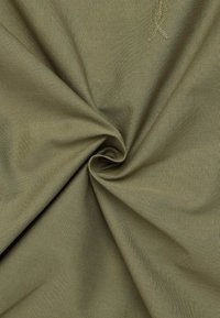 Khaki stof med en glat tekstur, der har en spiralfold. En diskret broderet bånddetalje er synlig på overfladen.