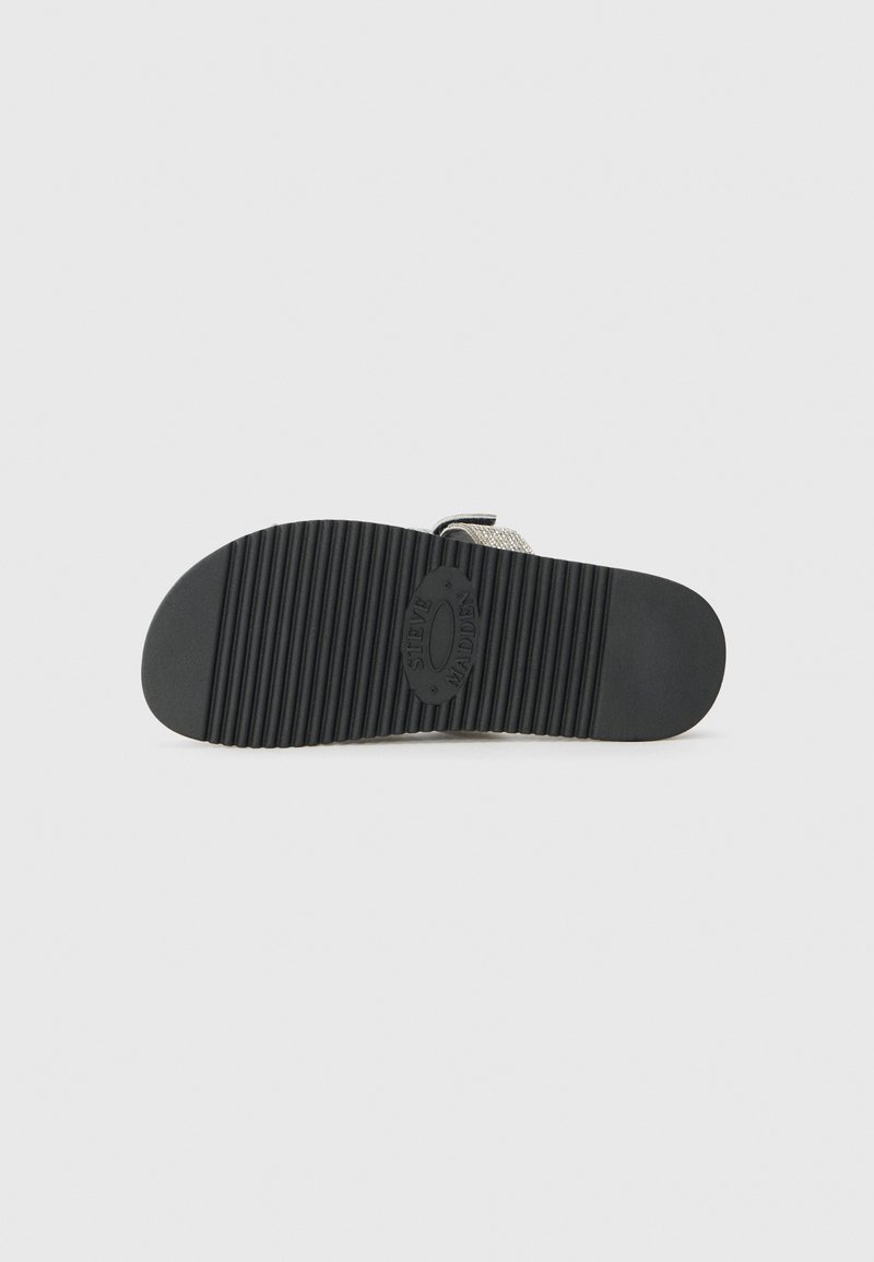 Semelle de chaussure noire en caoutchouc avec des rainures verticales, surface texturée et un logo rond au centre. Design minimaliste avec une forme plate.