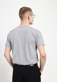 Šedé tričko s krátkým rukávem a kruhovým výstřihem, vyrobené z hladkého bavlněného materiálu, ve spojení s černými kalhotami, které mají dvě zadní kapsy.