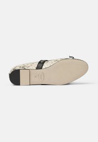 Sort hæl-sandal med en tekstureret beige indersål, der har en rem med en metalaccent og en solid sort hæl. Flad således design.