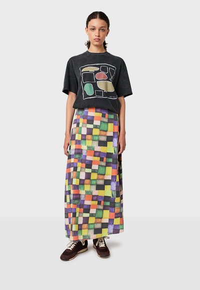 T-shirt graphique noir avec des formes colorées, associé à une jupe maxi à motifs multicolores. Caractéristiques : coupe décontractée et sneakers contrastants.