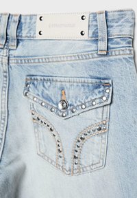 Poche arrière en jean bleu clair avec des clous métalliques, un rabat à bouton et un patch blanc de la marque Stradivarius au-dessus de la ceinture.