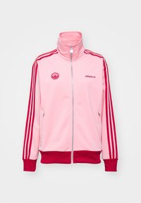 Růžová mikina na zip z tréninkového soupravy, se červenými pruhy, vysokým límcem, předními kapsami a nášivkou loga Adidas na hrudi.