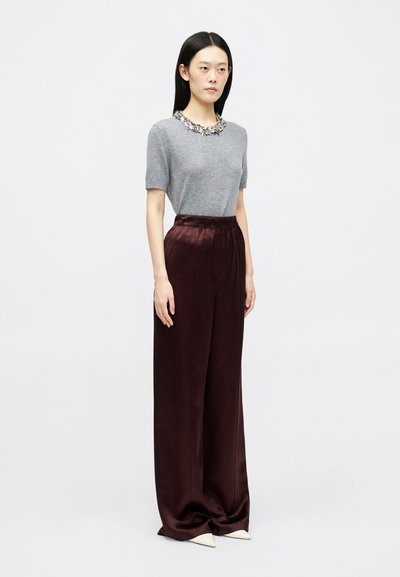 Siv majica s kratkimi rokavi z okrasnim ovratnikom, v kombinaciji z visoko pasom burgundskimi satenastimi širokimi hlačami in belimi čevlji s koničastim nosom.