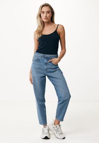 Schwarzes Tanktop, hoch geschnittene, hellblaue Jeans mit lockerer Passform und weißen Sneakers. Glatter Stoff, Knöchellänge und minimaler Detailgrad.