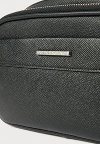 Juodas tekstūruotas dirbtinis odos krepšys su sidabriniu "Armani Exchange" logotipo plokštele. Uždarymas užtrauktuku su matomomis siūlėmis ir detalėmis.