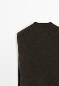 Maglione di lana marrone con collo alto, texture morbida e spacchi laterali per facilitare i movimenti. Design semplice senza hardware visibile.