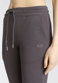 Lila Jogginghosen aus weichem Material, ausgestattet mit einem elastischen Bund und Kordelzug sowie seitlichen Taschen. "H.I.S" ist auf der Vorderseite gestickt.