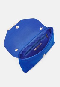 Bolso de mano de ante azul con un cierre de oro, broche magnético y bolsillo interior con cremallera. Presenta una textura suave y una forma sencilla.