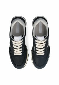 Baskets en mesh noires avec des lacets crème, un col rembourré et une semelle contrastante. Présente des motifs texturés et un logo simple sur la languette.
