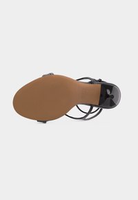 Σόλα μαύρου παπουτσιού με ψηλό τακούνι από γυαλιστερό δέρμα, με καφέ υφή αντιολισθητικής σόλας και λεπτές λουρίδες ορατές γύρω από τις άκρες.