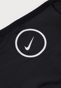 Tuvas plānotā melnā auduma tuvplāns, uz kura virsmas ir drukāts balts Nike swoosh logotips iekšā baltā aplī.