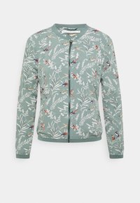 Grön bomberjacka med ett bladdesign och färgglada fågelmönster. Har en framzip och ribbade muddar och nederkant. Mjuk material.