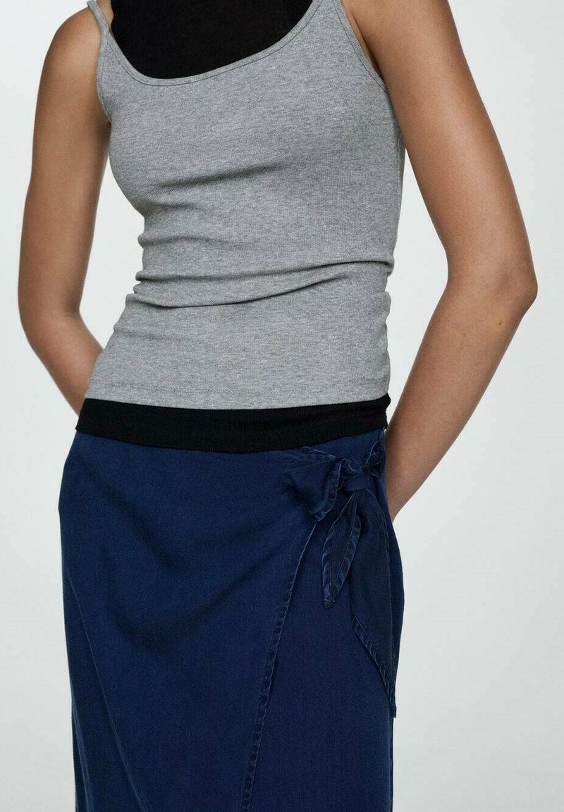 Débardeur gris ajusté avec des fines bretelles, associé à une jupe portefeuille bleu marine ornée d'un nœud à la taille. Tissu doux avec une légère texture.