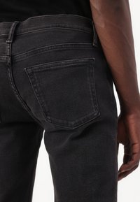 Jeans de mezclilla negra con un diseño de corte recto, que cuentan con un bolsillo trasero y detalles de costura sutiles. La tela tiene una textura suave.