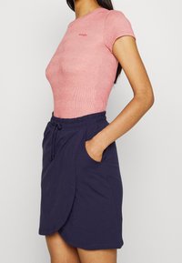 Červený pruhovaný top s krátkým rukávem v kombinaci s námořnickou zavinovací sukní s elastickým pasem a bočními kapsami. Hladké materiály celkově.