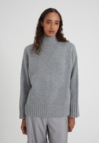 Pull en tricot gris avec un col montant, un ourlet côtelé et une coupe ample. Texture douce, manches longues et un design simple sans motifs.