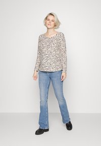 Top de manga longa com padrão de leopardo, feito de tecido macio, combinado com jeans flare de azul claro e botas de plataforma pretas. Textura plana e suave.