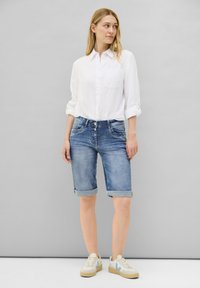 Shorts en denim bleu clair de style bermuda avec des poignets retroussés, associés à une chemise boutonnée en lin blanche. Comprend des poches avant et une coupe décontractée.