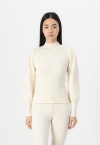 Pulover crem din tricot cu model de coaste, cu guler înalt și mâneci lungi bufante, având o siluetă ajustată și o țesătură texturată.