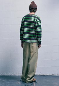 Pruhovaná košeľa s dlhým rukávom v čiernej, zelenej a bielej farbe, s voľnými khaki nohavicami. Obsahuje hnedú rebrovanú čiapku. Má predné vrecká a široký strih.