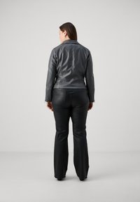 Μαύρο δερμάτινο μπουφάν με εφαρμοστή σχεδίαση, ορατές ραφές και ελαφρώς στενή μέση, σε συνδυασμό με μαύρα φαρδιά παντελόνια.