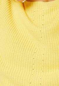 Gul stickad tröja med ribbat mönster och subtil vertikal sömmönster, delvis bärs av en person.