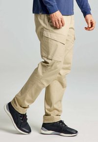 Beige cargobroek met meerdere zijzakken, gemaakt van katoen, rechte pasvorm, gecombineerd met gestructureerde zwarte sportschoenen.
