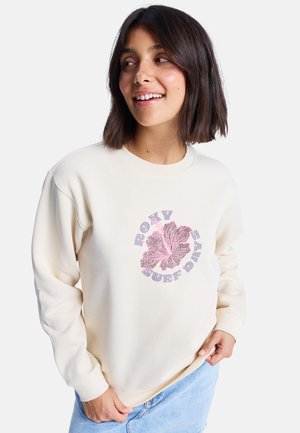 Crème-kleurige sweatshirt met geribbelde manchetten en halslijn. Heeft een roze bloemgraphic en de tekst "ROXY SURF DAYS" in een ronde vorm.