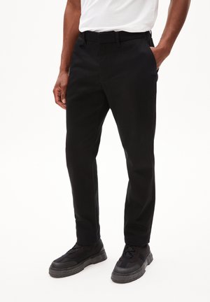 Zwarte broek, slim fit, gemaakt van gladde stof met riemlussen. Gepaard met zwarte sneakers met een chunky zool.