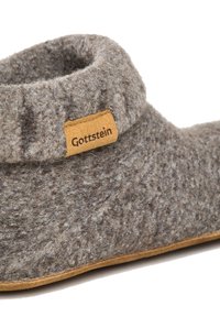 Pantofole grigie con una texture morbida, altezza bassa alla caviglia e un'etichetta in pelle marrone con la scritta "Gottstein". Presentano una suola sottile e flessibile.