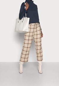 Maglione a collo alto navy abbinato a pantaloni larghi a quadri beige e stivali ankle crema. Borsa tote bianca con dettagli in metallo argentato.