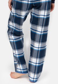 Pajama w kratę w kolorze granatowym, szarym i białym z niebieskimi akcentami. Wykonane z miękkiego materiału, o luźnym, prostym kroju i widocznych detalach szycia.