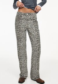 Jeans de pana leopardados hechos de denim, con un corte recto, diseño de cinco bolsillos y cierre de botón de latón. Los tonos de color incluyen beige y negro.