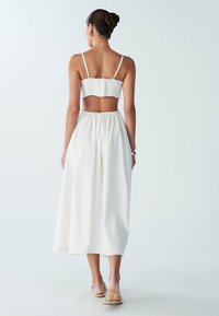 Top blanco corto con espalda fruncida y detalle de botones, combinado con una falda larga blanca y vaporosa. Tela suave y corte holgado, diseño de longitud hasta los tobillos.