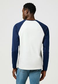 Raglan-Ärmel-T-Shirt in Weiß und Marineblau mit glatter Textur. Mit langen Ärmeln und Rundhalsausschnitt, entworfen für eine normale Passform.